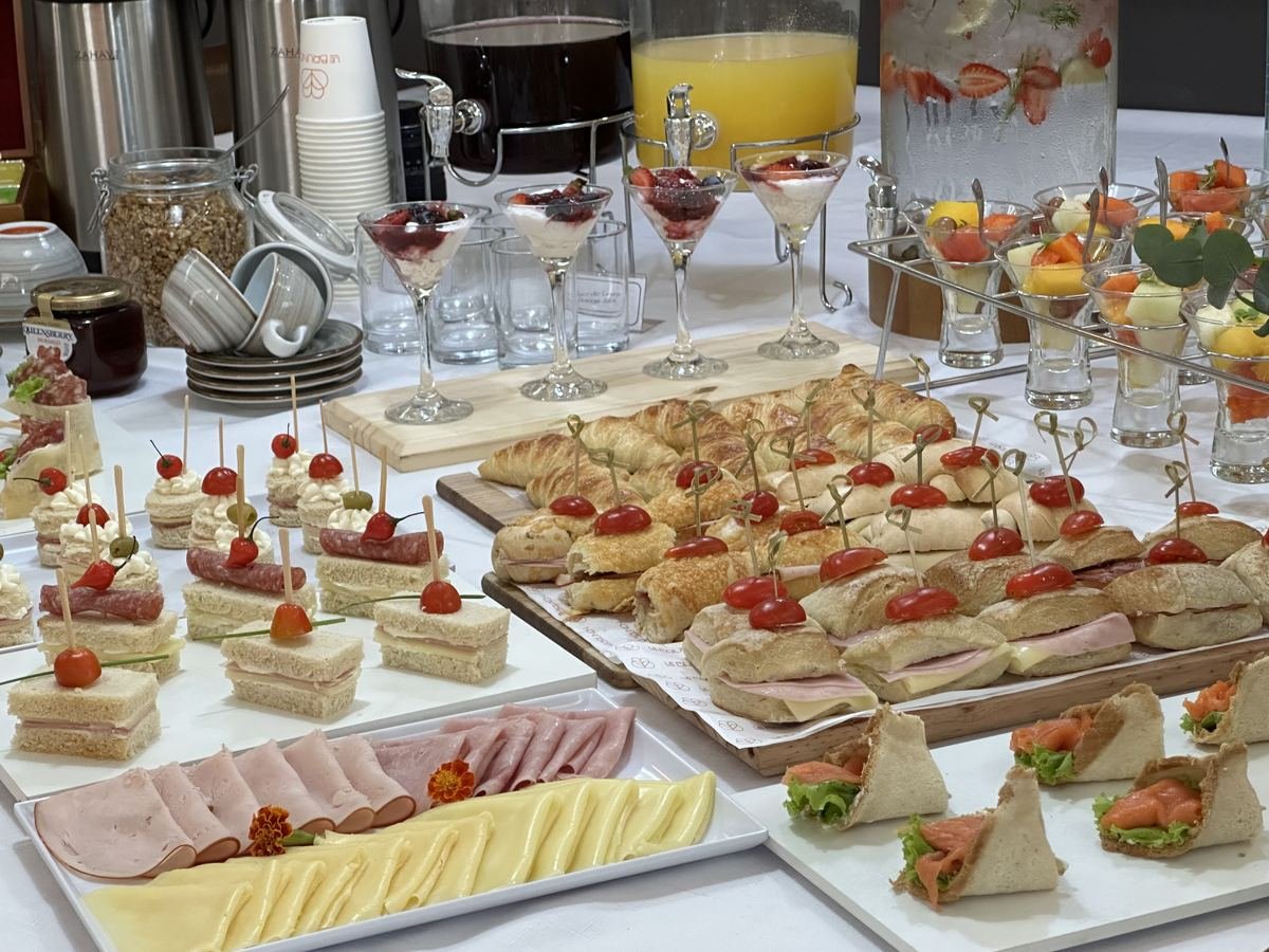 Mesa de coffee break corporativo com mini sanduíches, frios, queijos e sucos